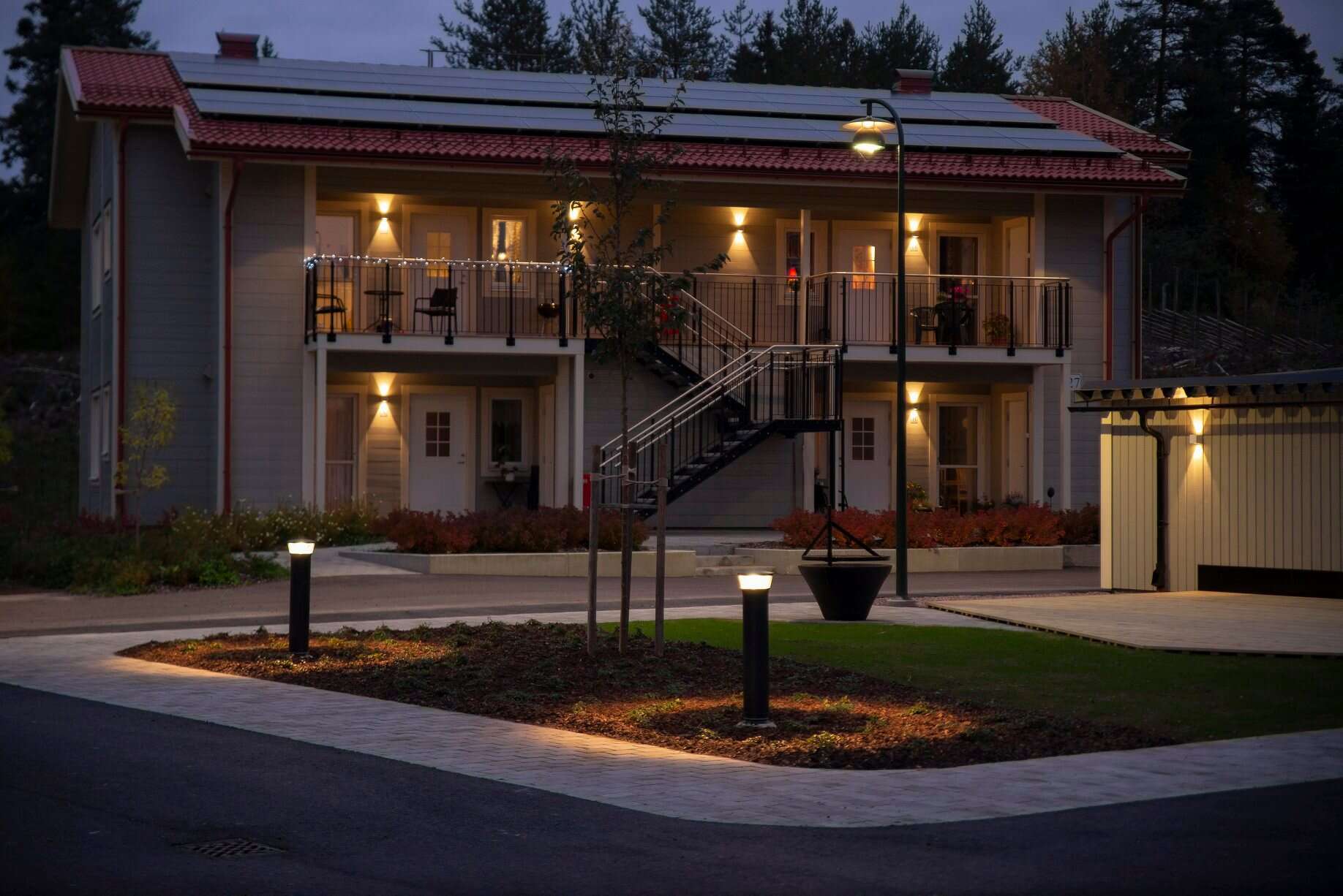 Vacker tvåvåningsvilla med utomhusbelysning och modern design, perfekt för familjeliv och avkoppling.