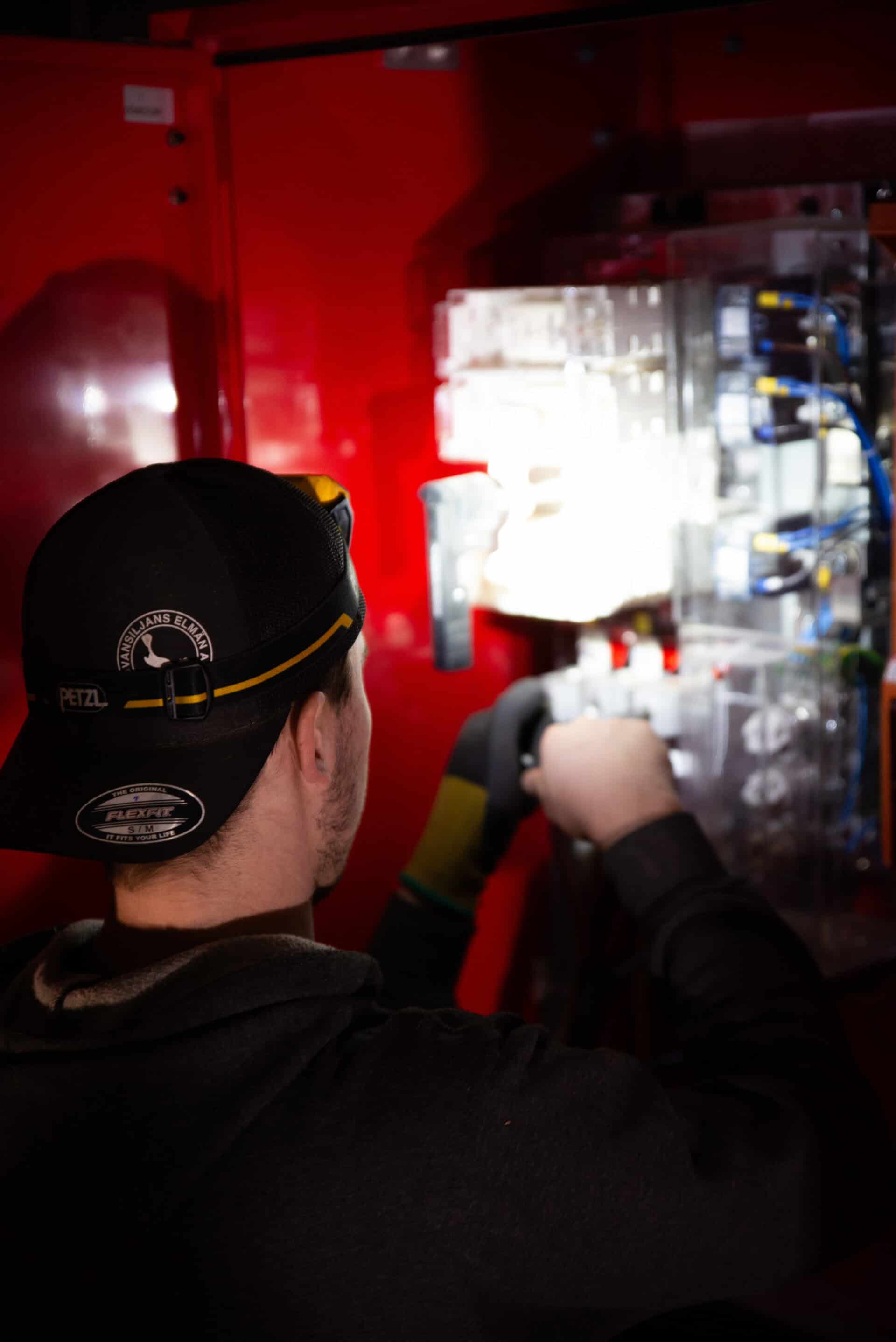 Elektriker installerar elcentral i röd elskåp för säker elförsörjning.