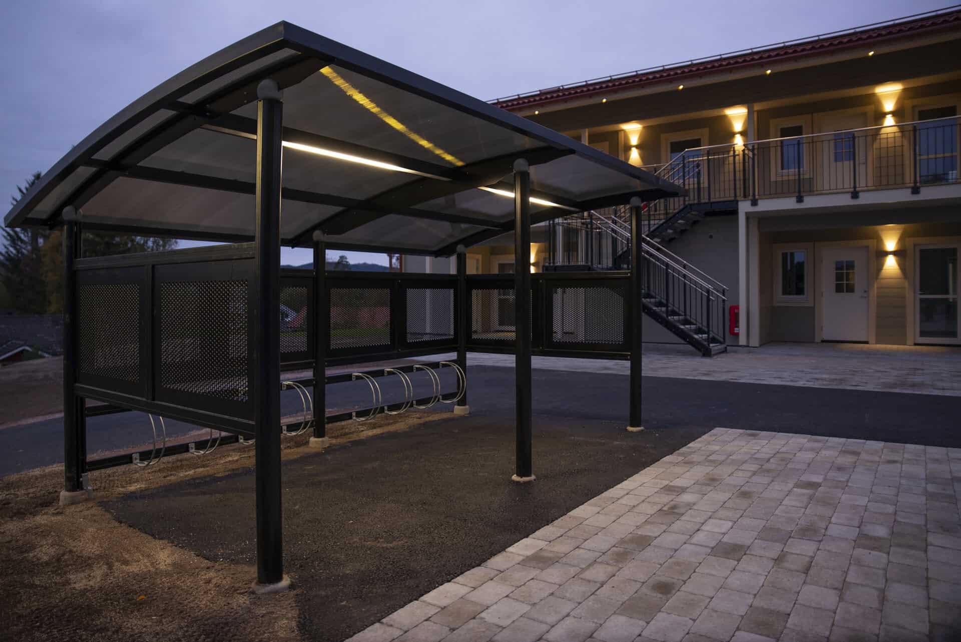 Busshållplats med tak och sittplatser vid Ovansiljans Elmän AB i kvällssol.