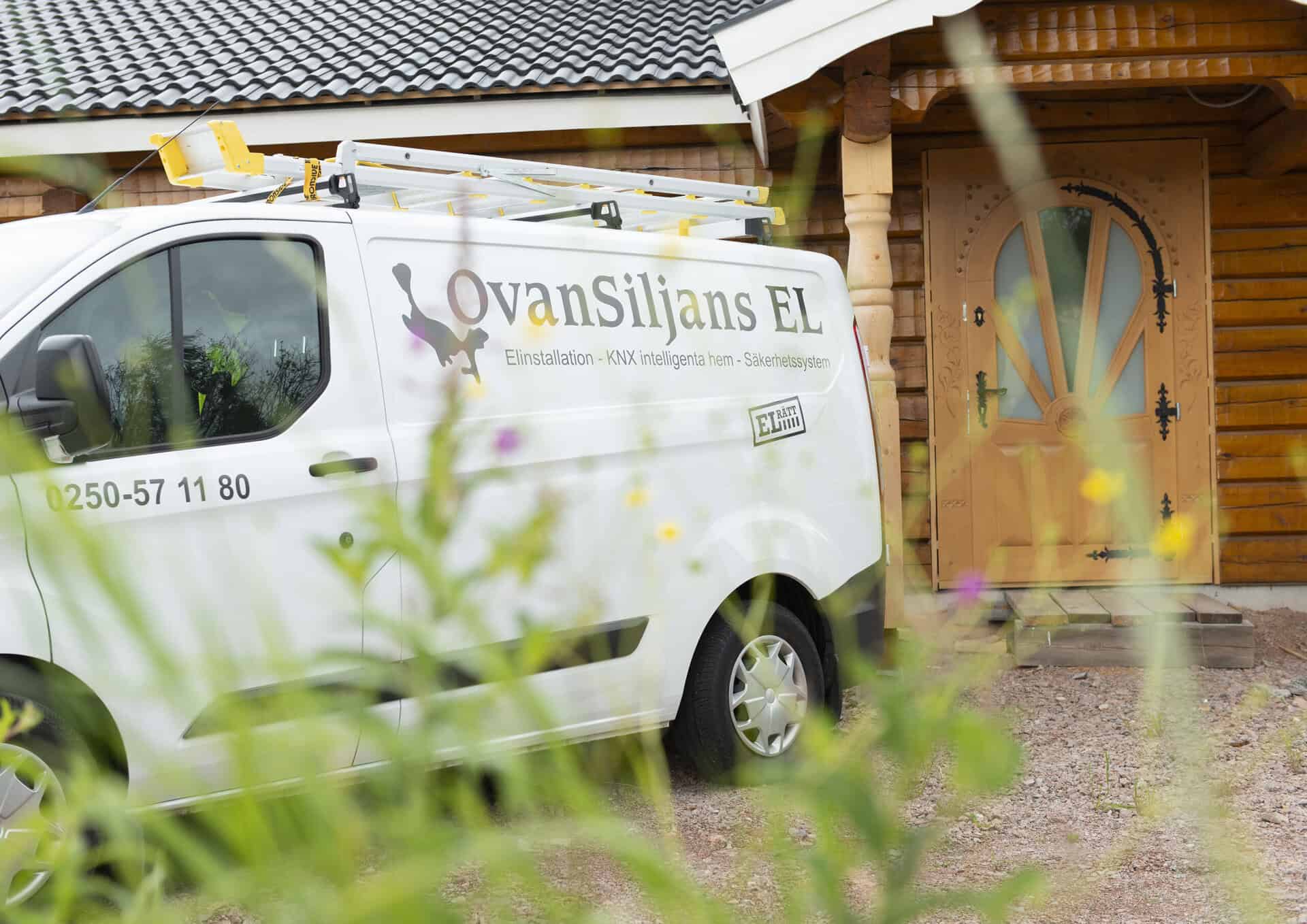 Elinstallationsbil för Ovansiljans Elmän AB utanför ett hus med träfasad.