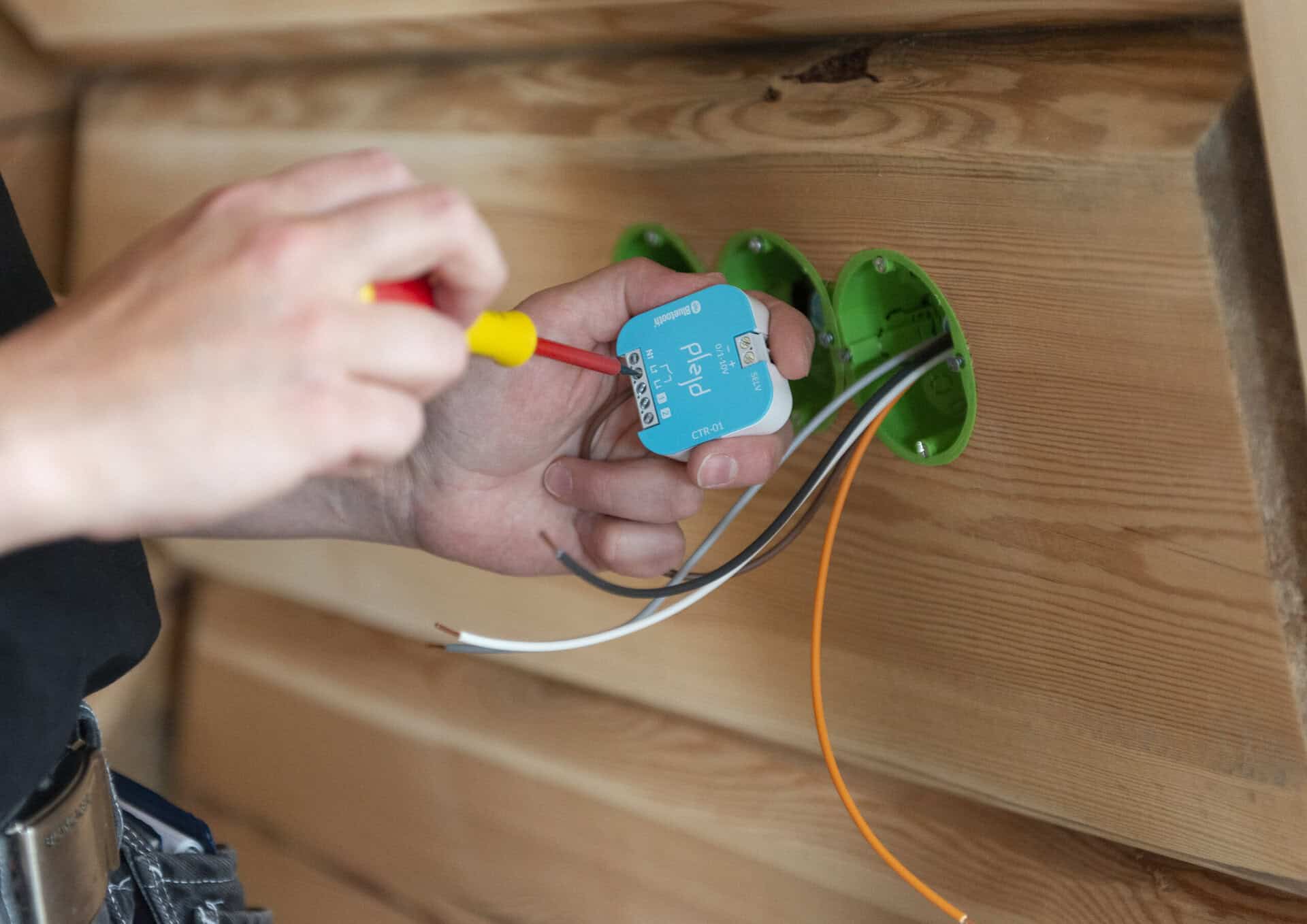 Person som installerar eluttag med verktyg i trävägg.